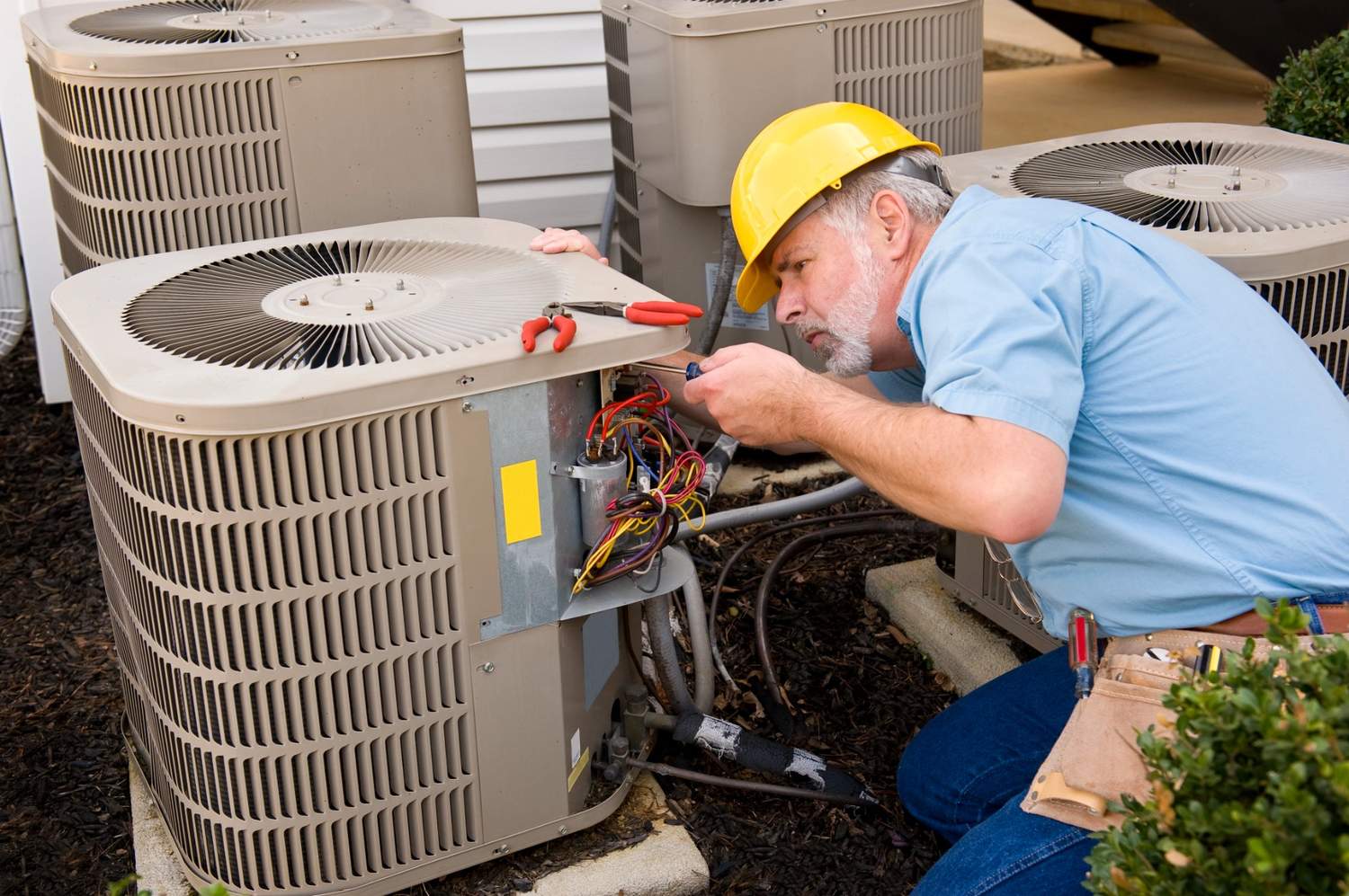 A technician in a yellow helmet performs fast air conditioner repair in Katy, TX, working on an outdoor AC unit with tools.