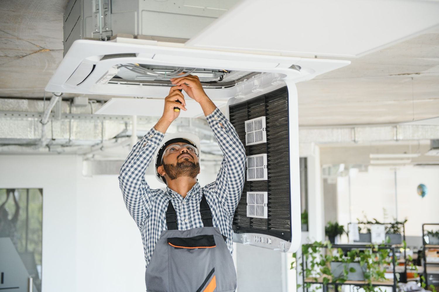 Technician in helmet and goggles performs emergency AC repair near me in Katy, TX, fixing ceiling-mounted unit in office space.