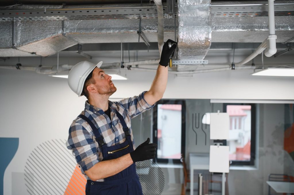 Technician in hard hat repairing an AC duct, offering 24/7 AC repair services in Katy, TX.