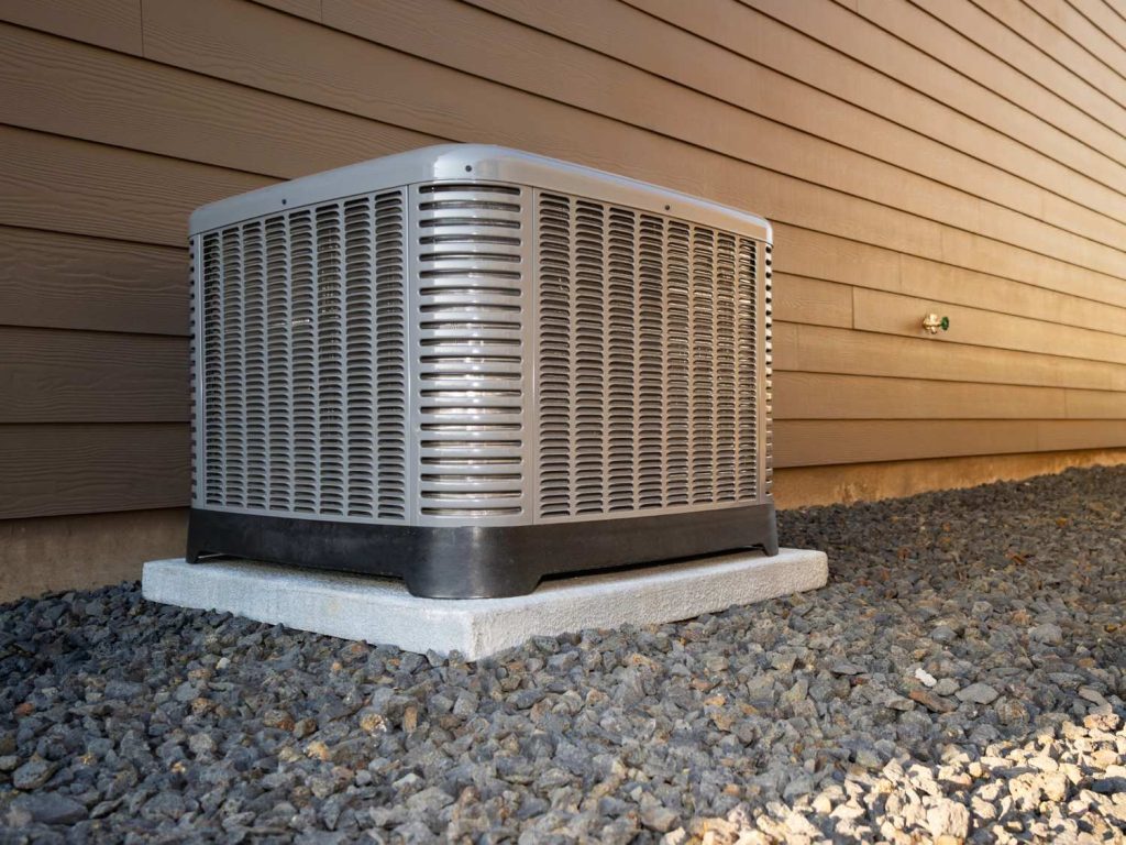 Outdoor AC condenser unit on gravel base next to house, for 24/7 AC repair services in Katy, TX.