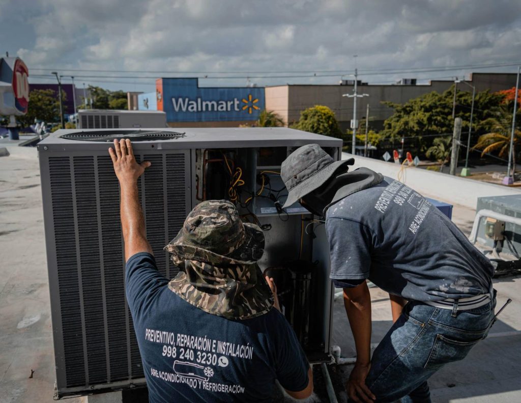 Two technicians maintain an energy efficient AC unit on a Katy TX rooftop, with Walmart store in the background.