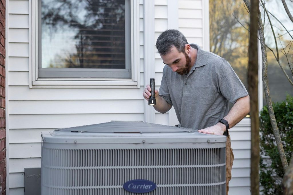Skilled technician inspecting an energy efficient AC unit outside a home in Katy TX, using a flashlight for detailed check.