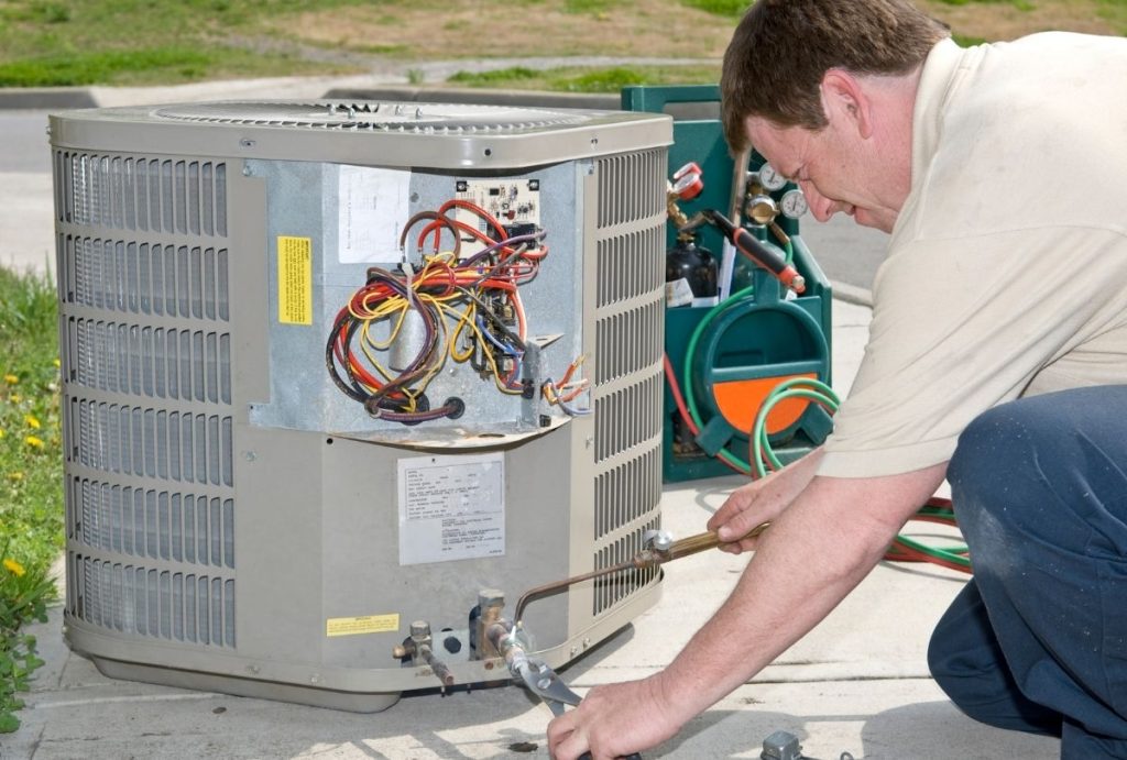 Expert technician examining wiring and components in an open air conditioner tune-up in Katy TX, focusing on safety and optimal performance.