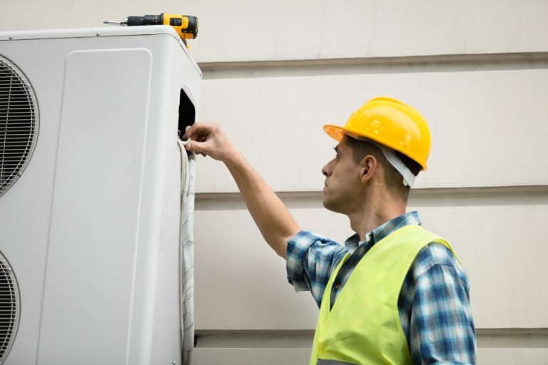 Professional technician performing AC maintenance Katy TX by using a screwdriver to service an outdoor cooling unit.