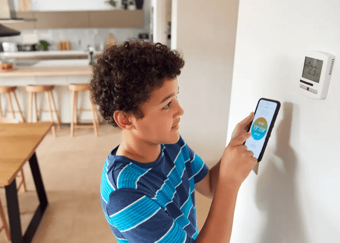 A young boy using a smartphone app to control a home unit after you upgrade to smart thermostats Katy Tx today.