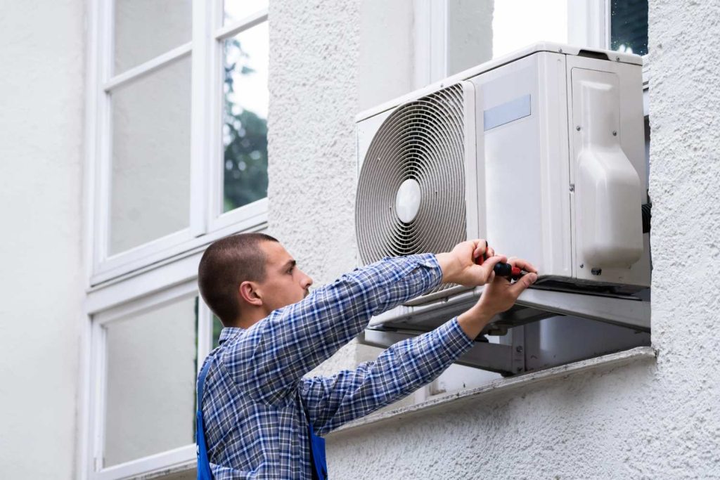 Technician using a screwdriver to provide emergency 24/7 AC repair Katy TX services on an outdoor mini-split unit.