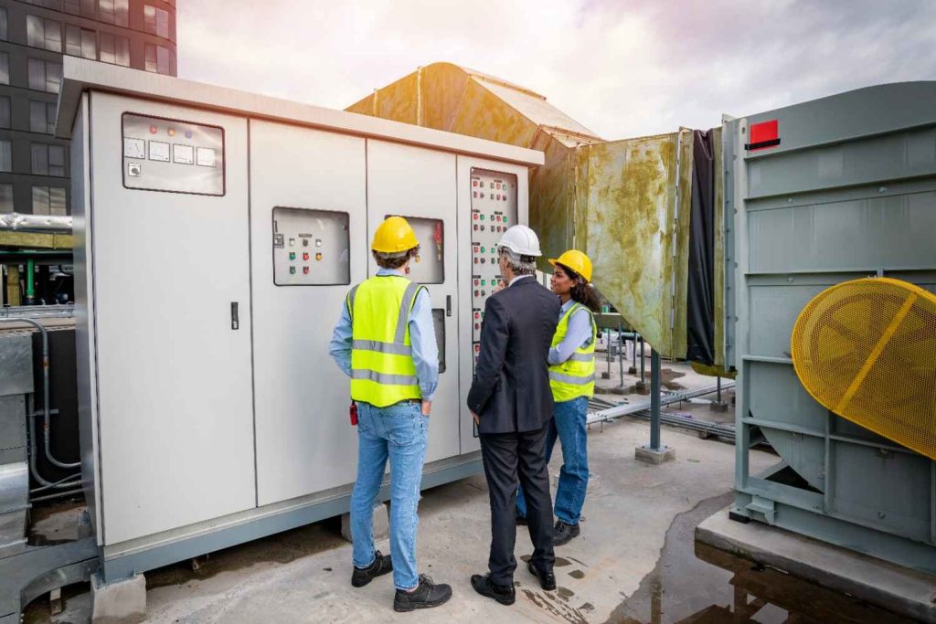 Managers consult with the best AC repair company in Katy TX beside a large rooftop HVAC control panel system. 