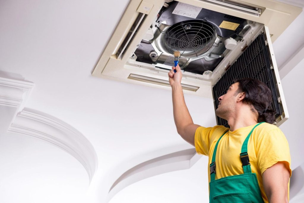Professional tech cleaning a commercial ceiling cassette system offering reliable 24/7 AC repair Katy TX services.