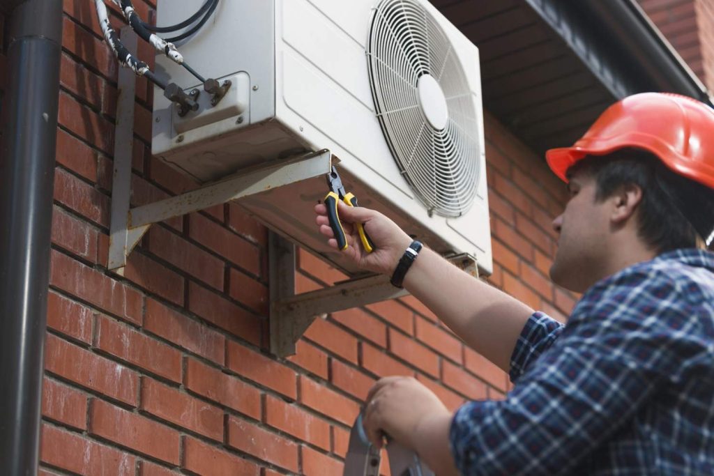 HVAC expert working on a brick wall mounted condenser unit for urgent 24/7 AC repair Katy TX homeowners count on.