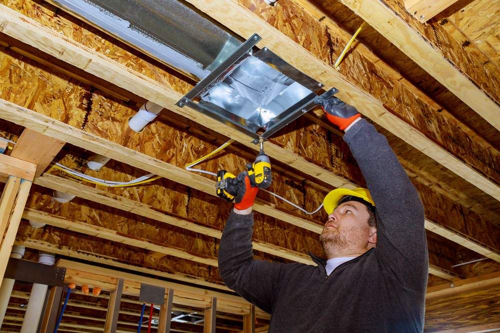 HVAC tech in hard hat installs metal duct collar in an unfinished attic. Complete AC repair Cinco Ranch and maintenance.